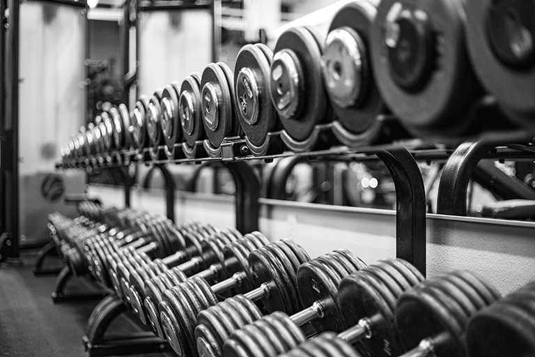 Black and white photo of dumbells on rack. Foreground in focus, with a gradient blur towards background.